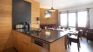 Eine moderne Küche mit Kochinsel, Holzwandverkleidung und einem Essbereich mit einer Couch und Stühlen.
