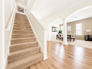 A staircase leading to a dining area with a high ceiling and wooden flooring.