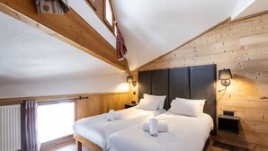 Una habitación con dos camas, paredes de madera, una ventana con cortinas y una lámpara fijada a la pared.