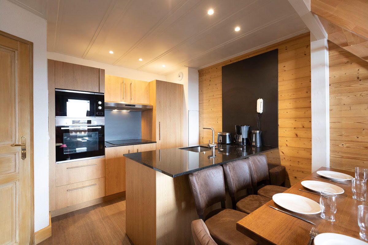 Une cuisine moderne avec des meubles en bois, un four encastré et un coin repas comprenant une table et des chaises en bois.