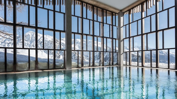 An indoor swimming pool with large windows offering a view of snow-covered mountains.