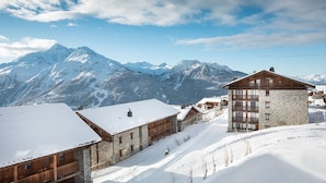 A snow-covered mountain village with stone buildings and wooden structures, featuring a prominent stone building with balconies.