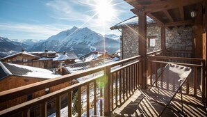 A wooden balcony with a stone wall, overlooking snow-covered mountains and a clear sky.