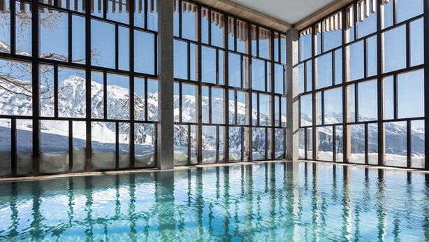Piscina interior con amplios ventanales que ofrecen vistas a montañas nevadas.