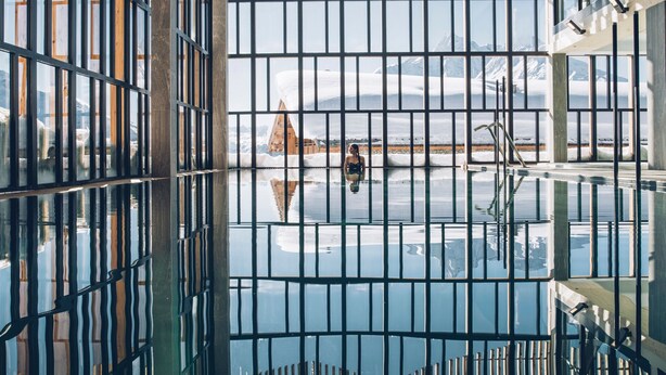 A room with large windows, a view of a snowy landscape, and a reflection of the scenery in the glass.