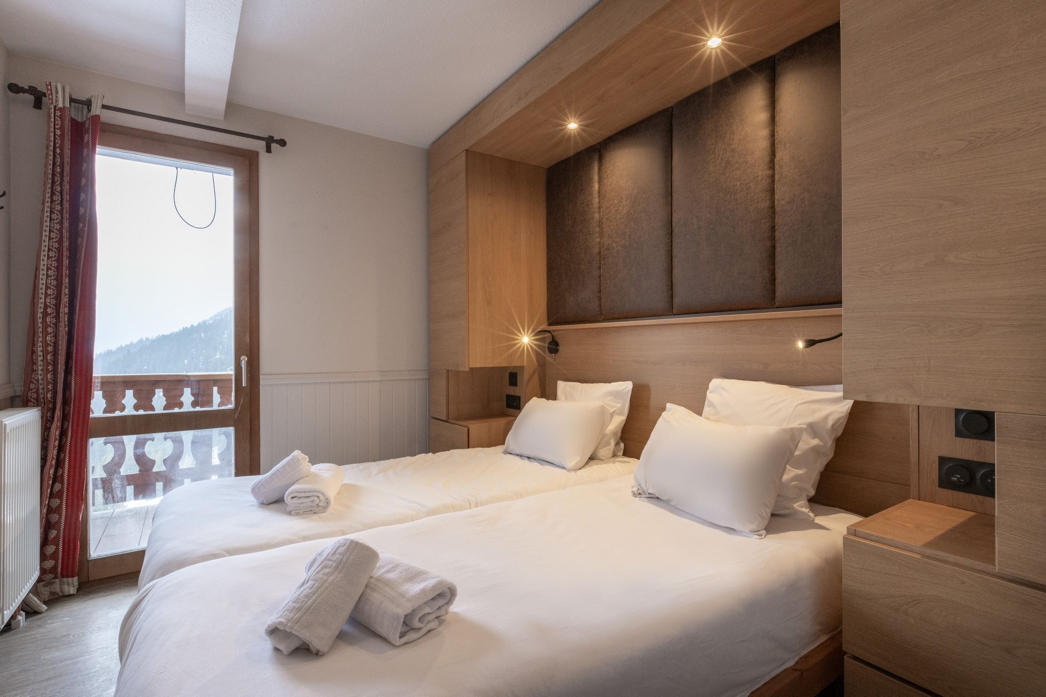 Une chambre d’hôtel avec deux lits, des têtes de lit en bois, des tables de chevet et un balcon avec vue.