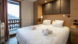 Hotellihuone, jossa on suuri sänky, kaksi yöpöytää, yölamppu, ikkuna verhoilla ja näkymä ulkona olevaan rakennukseen.