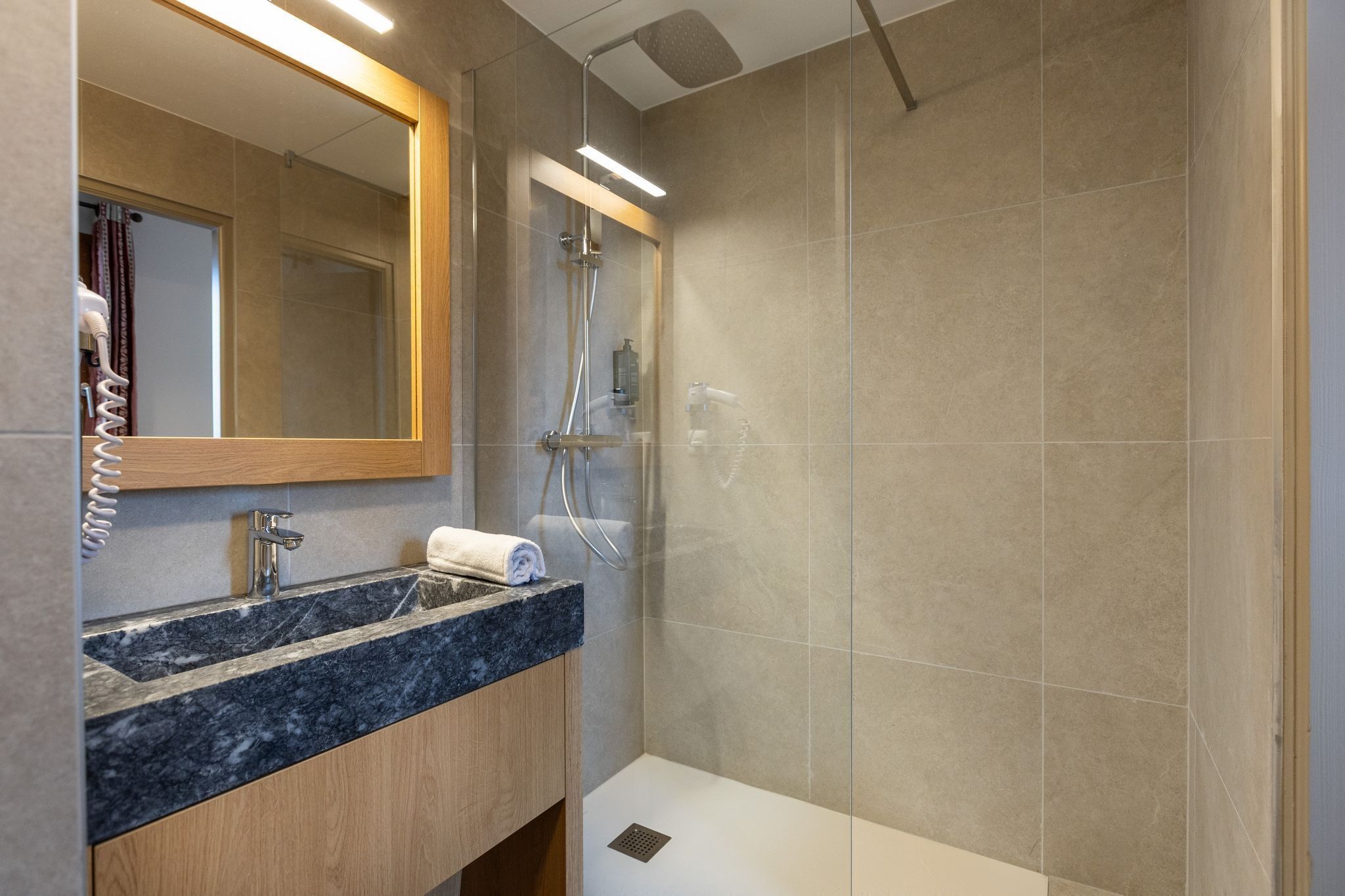 A modern bathroom with a marble sink, a glass-enclosed shower, and a wooden vanity.