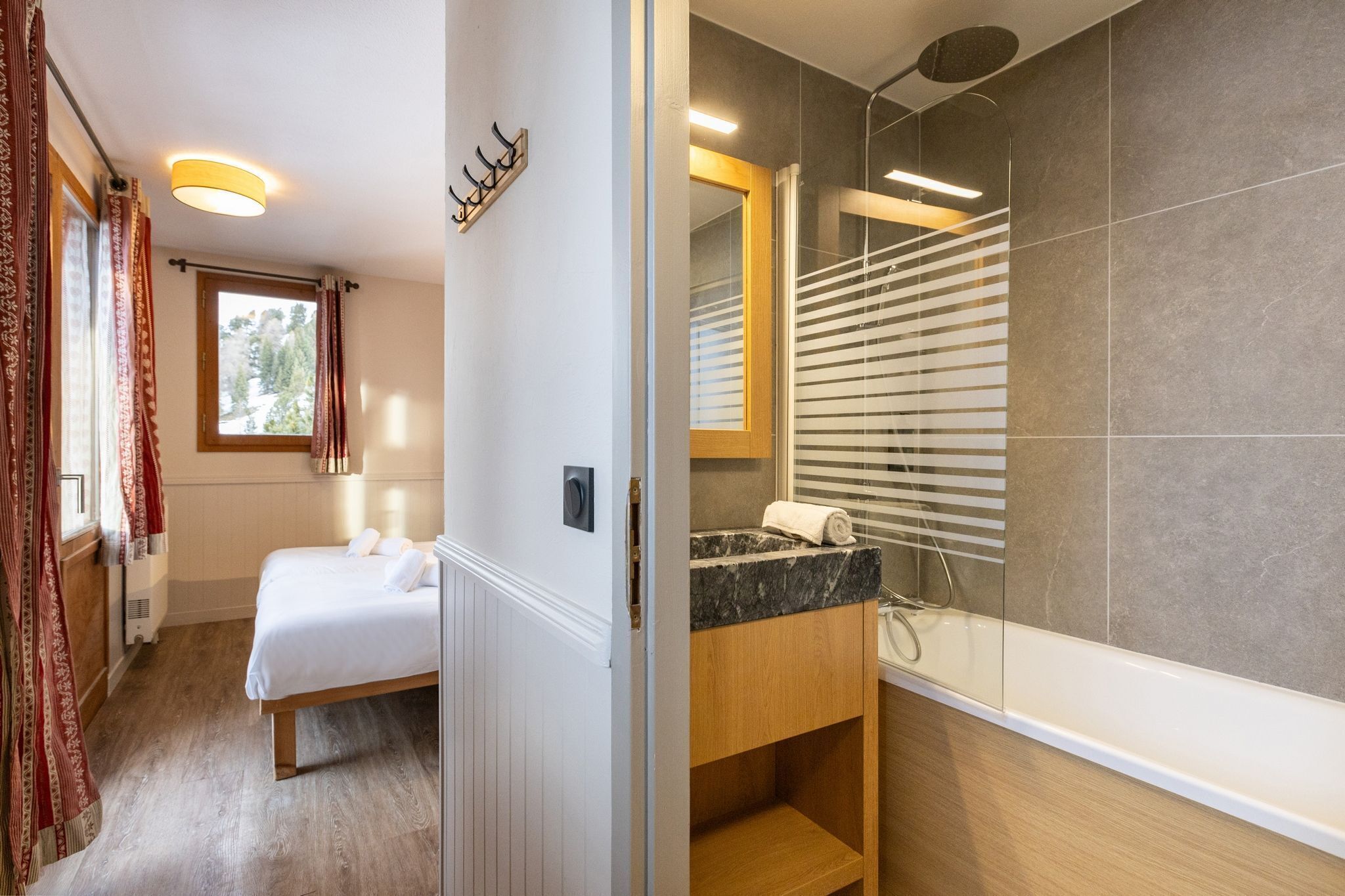 Ein modernes Hotelzimmer mit Bett, einem Badezimmer mit großem Spiegel und einem Fenster mit Vorhängen.