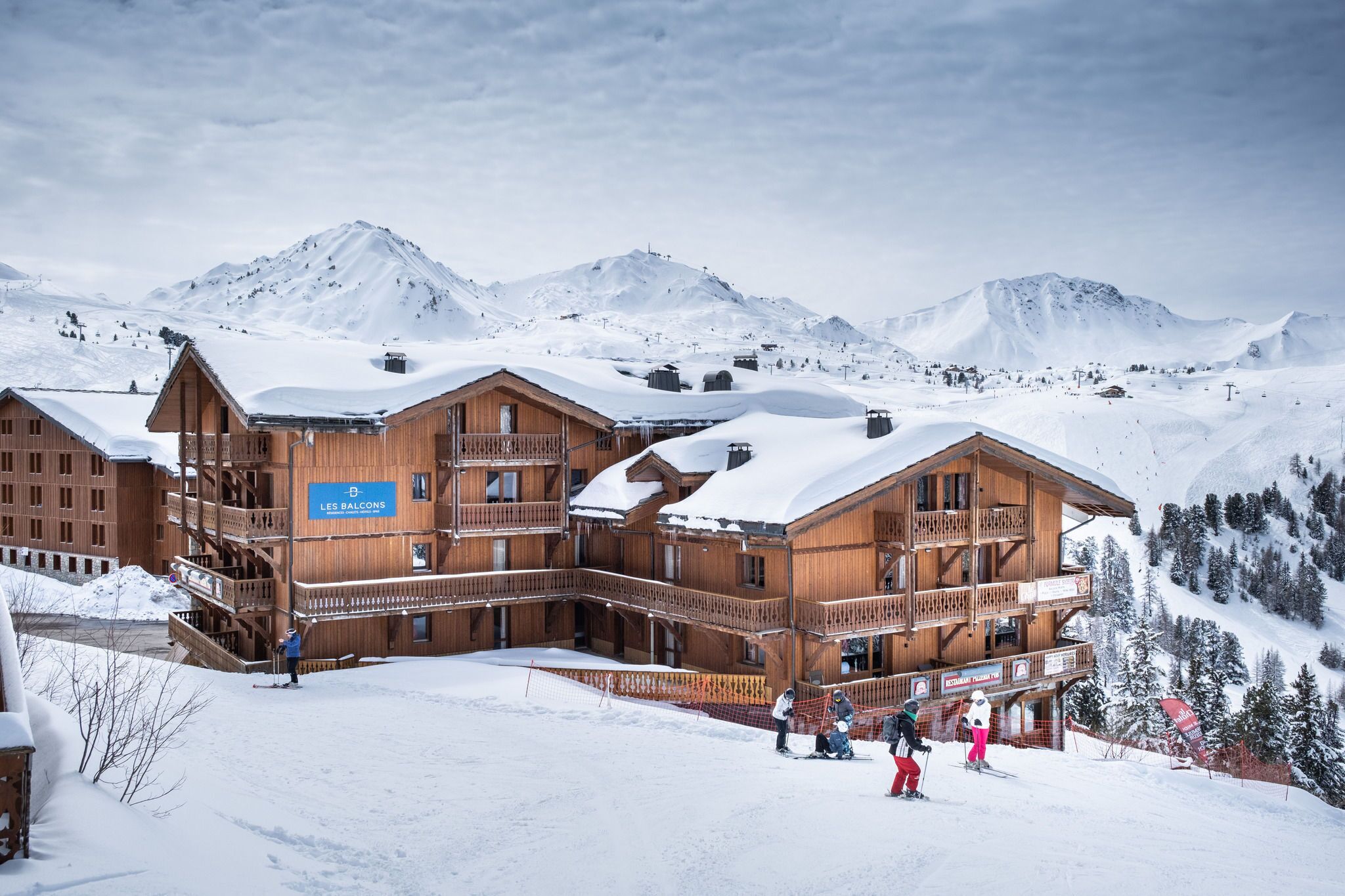 A wooden chalet with multiple balconies, surrounded by snow-covered mountains.