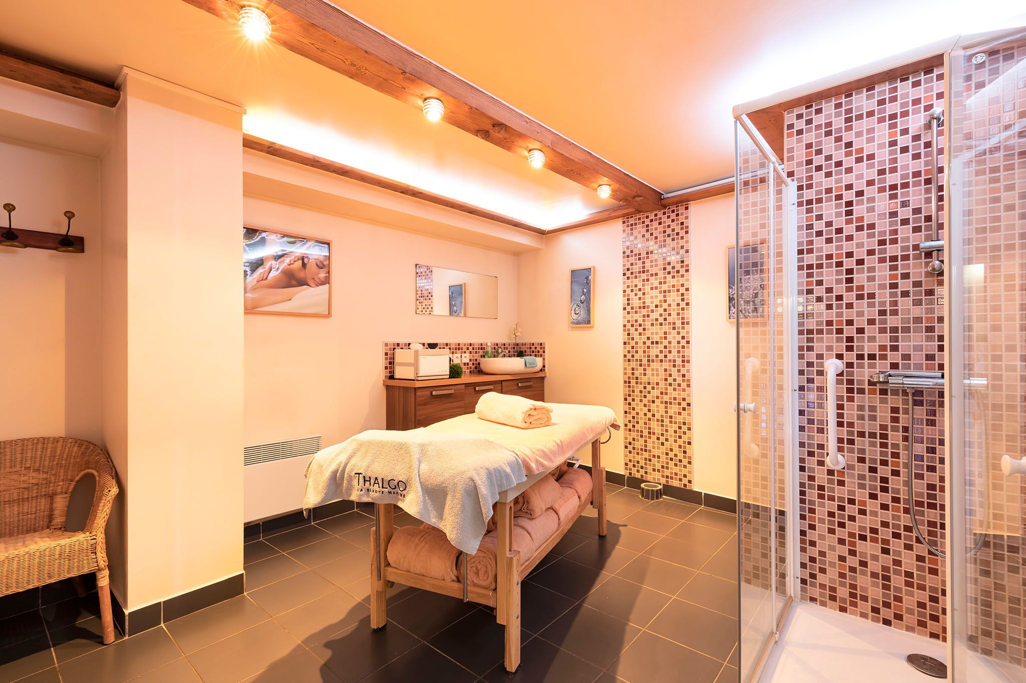 A spa room with a massage table, a shower area, and a wicker chair.