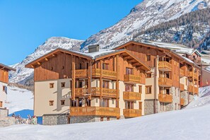 Un edificio de madera de varios pisos con balcones, probablemente un hotel, con una imponente montaña nevada de fondo.