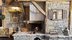 Une cheminée en pierre avec un feu de bois, des poutres apparentes et un mur en pierre rustique.
