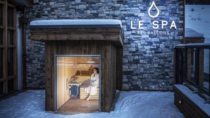 A spa entrance with a stone facade and wooden elements, including a wooden door and a bench outside.
