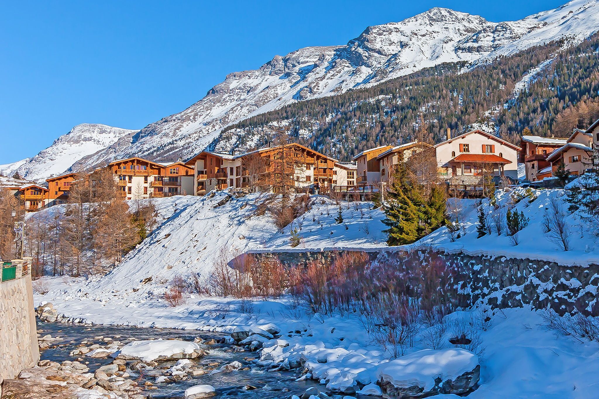 Un complejo turístico de montaña con edificios de madera, un río y montañas nevadas.