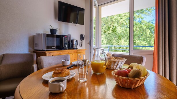 Una mesa de desayuno con cruasanes, café, jugo y fruta, además de un televisor, un microondas y un teléfono.
