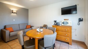Un espacio habitable compacto con sofá, mesa de comedor y televisor montado en la pared.