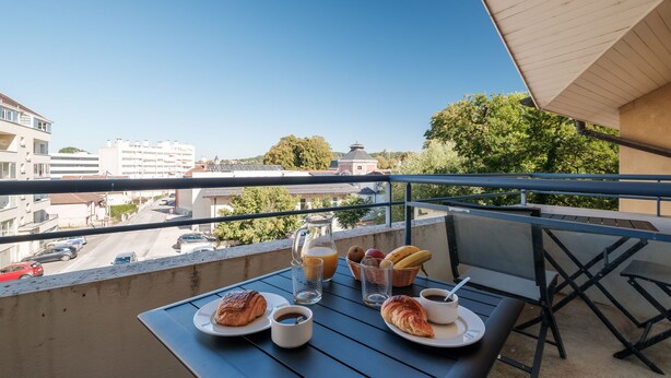 A balcony with a table set for breakfast, including croissants, coffee, and fruit.