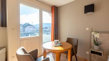 Une pièce moderne avec une table ronde en bois, deux chaises, une orchidée en pot et une vue sur les immeubles par une grande fenêtre.