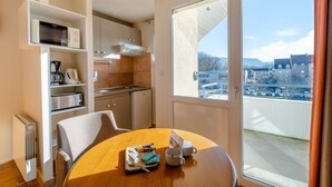 A compact kitchen with a microwave, toaster, and coffee maker, a dining table with a tray of breakfast items, and a large window with a city view.