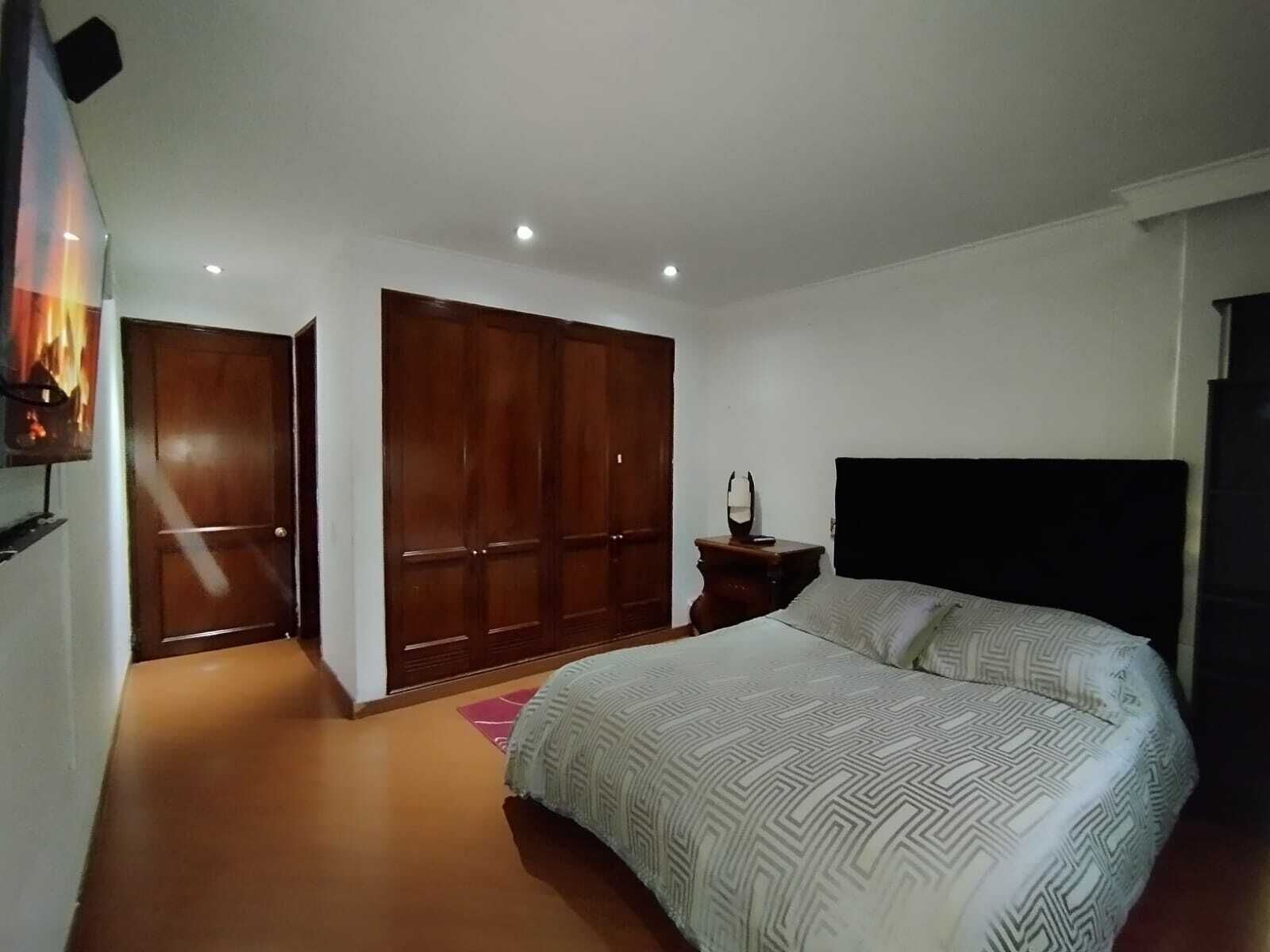 Un dormitorio con cama, armario, mesita de noche y televisor en la pared.