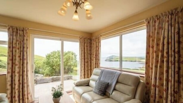 Una habitación con sofá frente a amplios ventanales, una pequeña mesa con una planta y vistas a zonas verdes y agua.