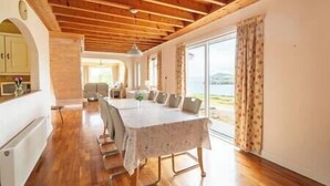 Un comedor con una mesa larga y sillas, piso de madera y vistas al exterior.