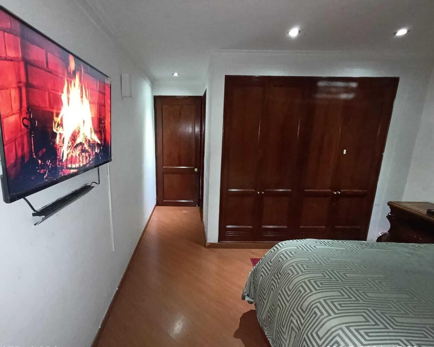Un dormitorio con televisión mostrando una chimenea, una puerta de madera y una cama con colcha estampada.