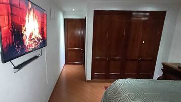 Un dormitorio con televisión mostrando una chimenea, una puerta de madera y una cama con colcha estampada.