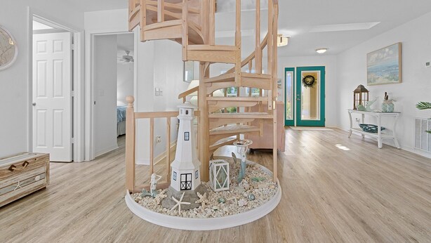 Eine Wendeltreppe mit einem Leuchtturm-Modell am Fuß, Holzdielen und einer grünen Tür im Hintergrund.
