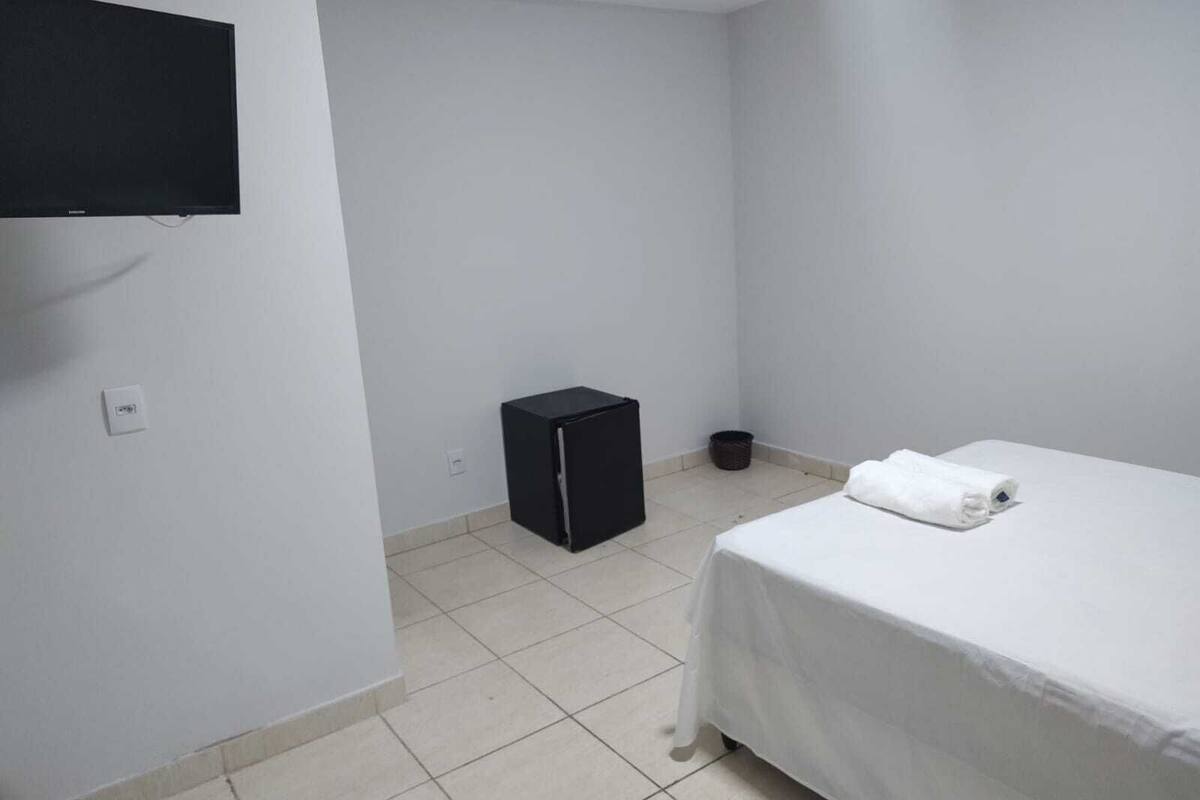 A small, clean room with a bed, a black cabinet, and a television mounted on the wall.