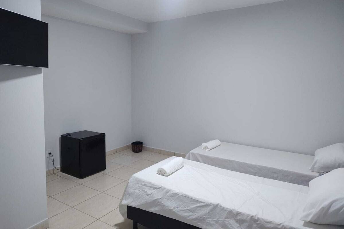 A small, clean room with two beds, a black speaker, and a trash bin.