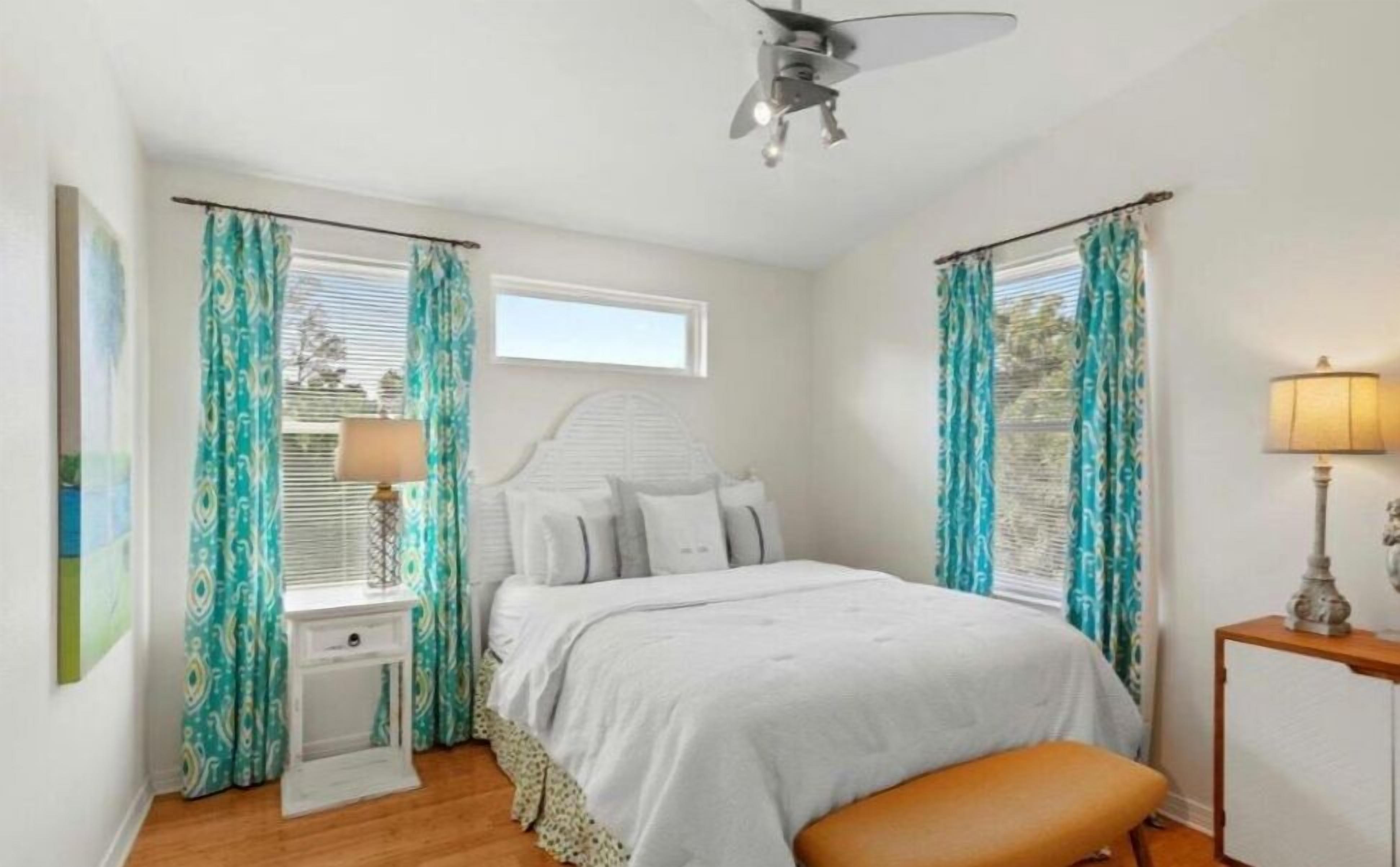 A bedroom with a bed, a nightstand, a lamp, a ceiling fan, and curtains.