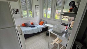 A compact bedroom with a bed, a small table, a sink, and a window with blinds. - Les Glycines - studio 9m2 cosy et reposant 1p (Arras)