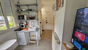 A compact kitchen with a sink, microwave, and small refrigerator. A television is mounted on the wall, and a door leads to another room. - Les Glycines - studio 9m2 cosy et reposant 1p (Arras)