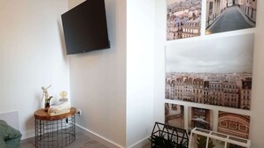 Un soggiorno moderno con una TV a parete, un tavolino rotondo in legno con libri e una scultura, e un muro decorato con fotografie di paesaggi urbani.