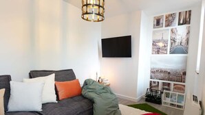 Un soggiorno moderno con un divano grigio, una TV a schermo piatto e una collezione di fotografie di paesaggi urbani alle pareti.