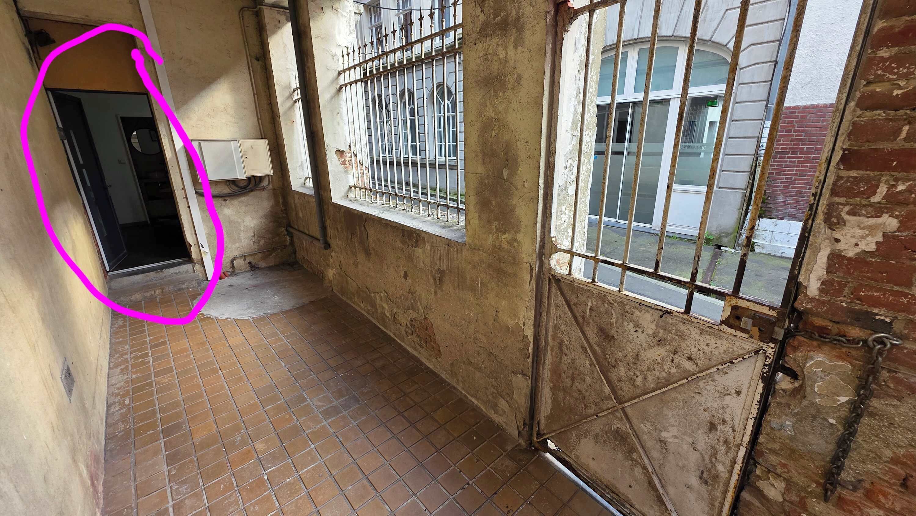 A narrow corridor with tiled flooring, a barred window, and a visible door leading to another room.