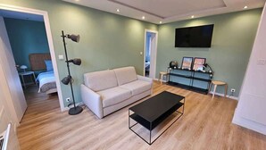 Un salon comprenant un canapé, une table basse, un lampadaire et un téléviseur fixé au mur.