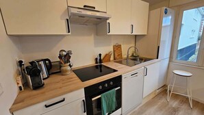 Une cuisine moderne avec des meubles blancs, une cuisinière noire, un évier et une fenêtre donnant sur un paysage urbain.