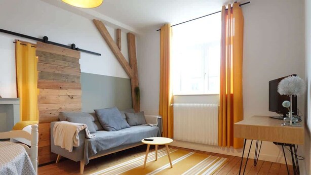 A modern living room with a sofa, a small round table, and a TV on a wooden stand. - L'Échappée Boisée Arrageoise • 2 ch • Gare (Arras)