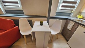 Eine kompakte Küchenzeile mit einem weißen Tisch und Stühlen, einem roten Sofa und einem kleinen Kühlschrank.