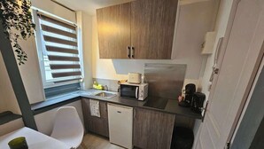 Eine kleine Küche mit Mikrowelle, Toaster und Kühlschrank. Ein Essbereich mit einem weißen Tisch und einem Stuhl ist ebenfalls vorhanden.