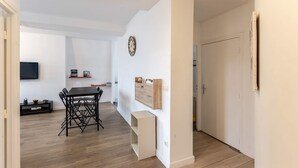 A modern living room with a dining table, chairs, a TV, and a wall-mounted clock. - Villa Arrageoise • Parking • hypercentre • 3e étage (Arras)