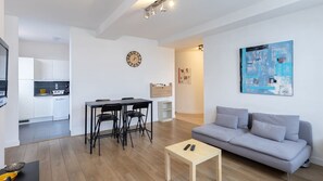 A modern living space with a dining area, a sofa, a coffee table, and a kitchen in the background. - Villa Arrageoise • Parking • hypercentre • 3e étage (Arras)