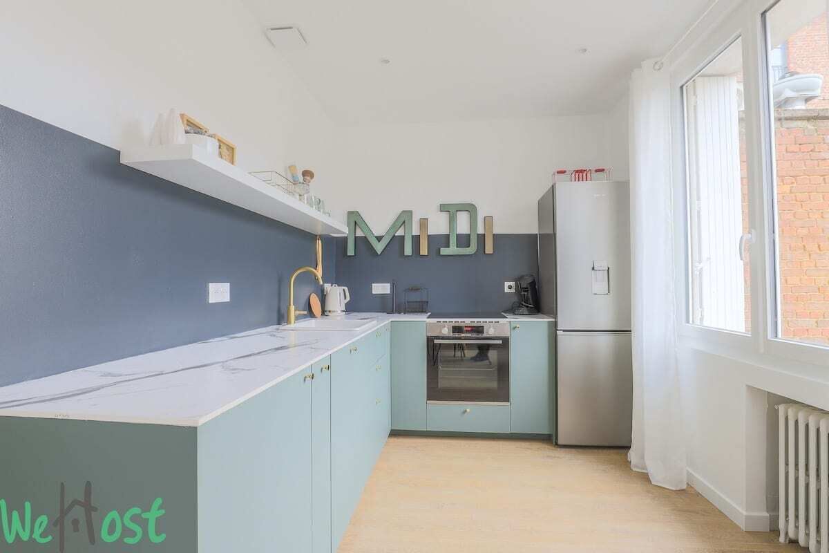 A modern kitchen with light blue cabinets, a stainless steel oven, and a refrigerator.