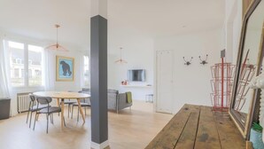 Ein moderner Wohnraum mit Essbereich, einer Couch, einem Fernseher und einer roten Metallskulptur.