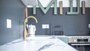 Eine moderne Küche mit weißer Arbeitsplatte, einem goldenen Wasserhahn, einem Bosch-Backofen und einem an der Wand befestigten Wasserkocher.