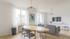 Ein modernes Wohnzimmer mit einem runden Holztisch, einem grauen Sofa und einem an der Wand montierten Fernseher.