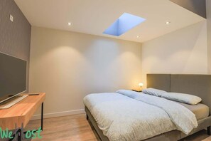 A modern bedroom with a bed, a desk, and a TV.